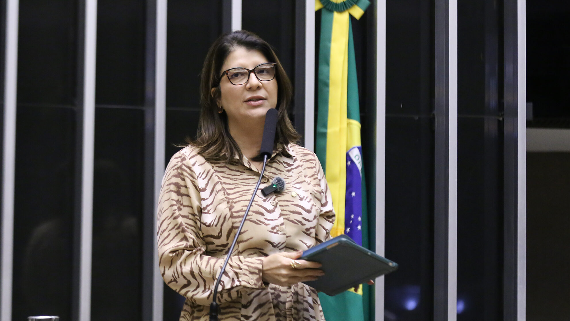 Carla Dickson, de óculos e blusa estampada, discursa no plenário da Câmara dos Deputados