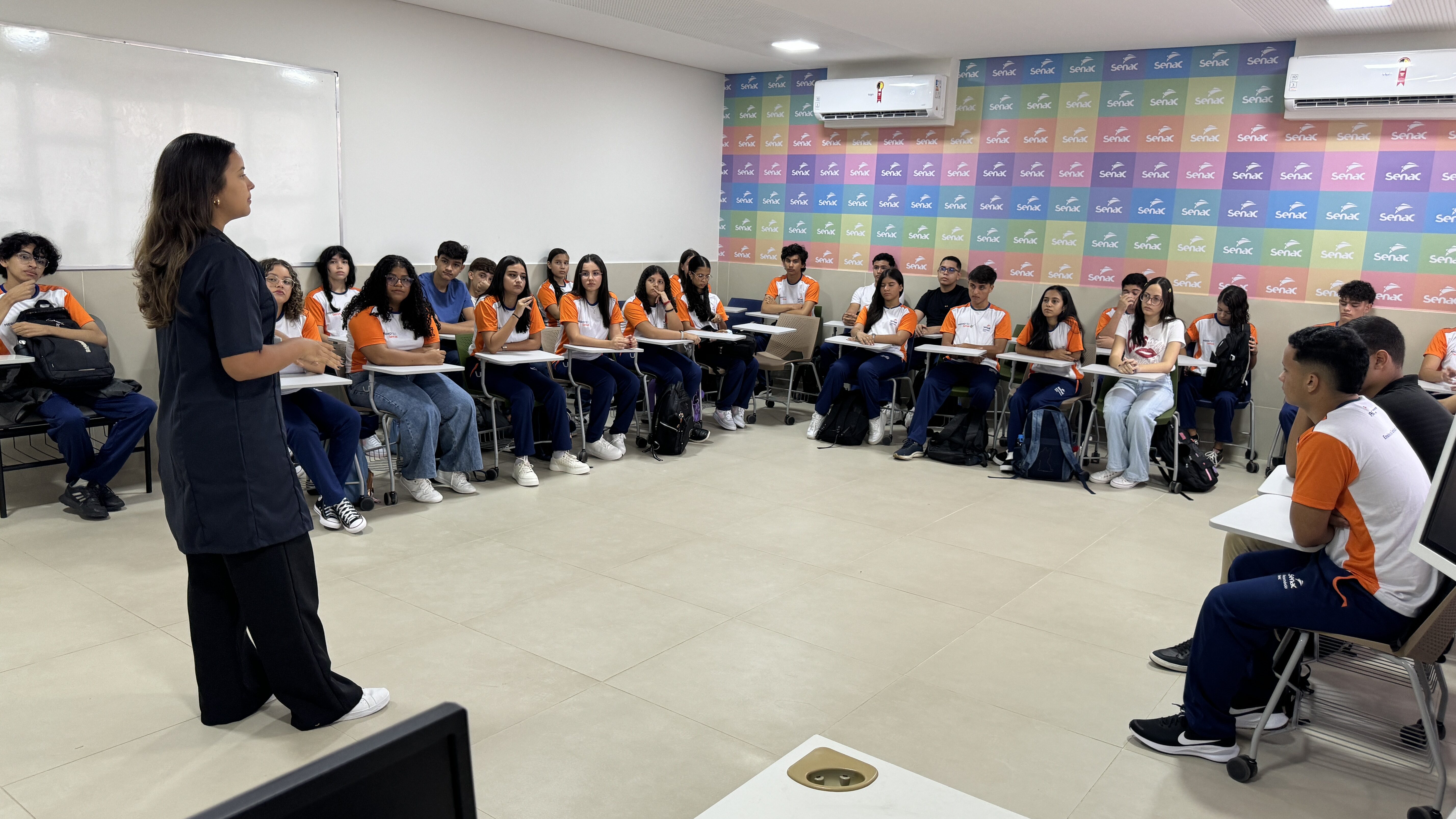 Estudantes sentados em carteiras dispostas em círculo numa sala de aula