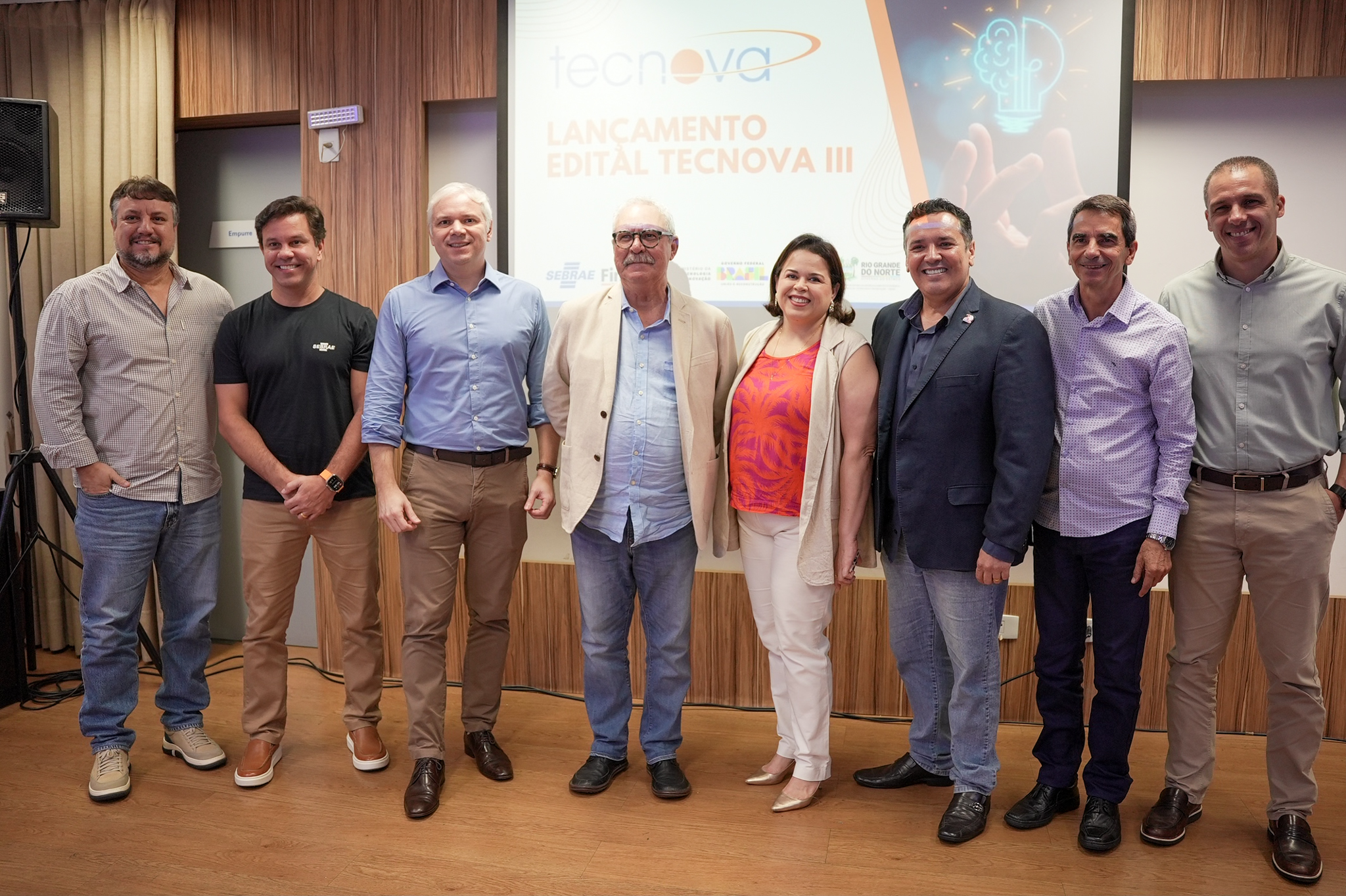 Participantes do lançamento do Tecnova III posam diante de painel do programa no Sebrae-RN em 2024